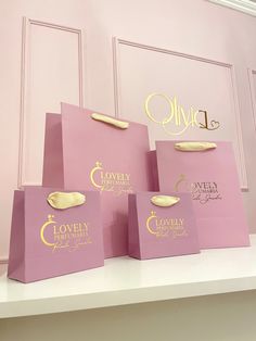 four pink shopping bags with gold lettering on them