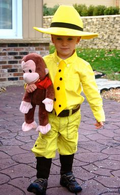 a little boy dressed up as a fireman with a monkey in his hand and wearing a yellow hat