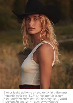 a woman wearing a black cowboy hat and red skirt standing in front of tall grass