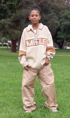 a young boy standing in the grass with his hands on his hips and wearing sweatpants