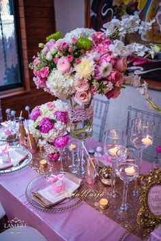 the table is set with pink and white flowers in vases, candles, and napkins