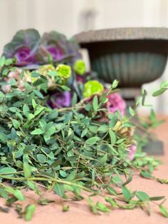 some green leaves and purple flowers on a table next to a bowl with a plant in it