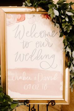 a welcome sign with flowers and greenery on it is displayed in front of a gold frame