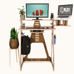 a computer desk with two computers on it and a plant in front of the monitor