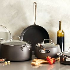 pots and pans are sitting on the counter next to wine bottles, garlic, and tomatoes