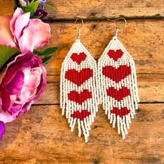 two red and white beaded earrings next to pink flowers on wooden table with purple peonie