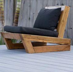 a wooden chair sitting on top of a wooden deck next to a fence with black pillows