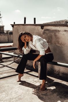 a woman is sitting on a ledge with her hand in her ear and looking at the camera