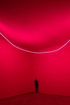 a person standing in an empty room with red lighting on the walls and flooring