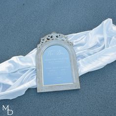 a wedding photo frame laying on the ground next to a white satin draped cloth,