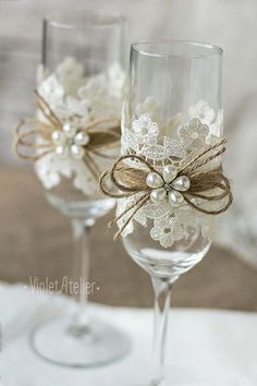 two wine glasses decorated with bows and pearls are sitting on a white cloth tablecloth