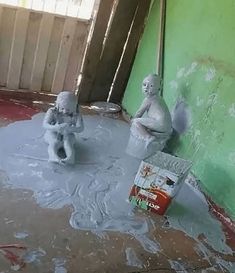 two little statues sitting on top of a dirty floor next to a can of soda