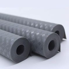 three rolls of gray fabric sitting next to each other on top of a white surface