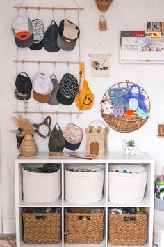 a white shelf with baskets and hats hanging on it's wall next to other items