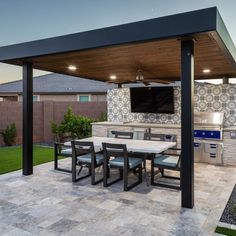 an outdoor kitchen and dining area with a television on the wall, grilling table and chairs