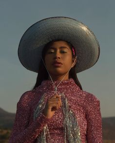 a woman wearing a large hat with tassels around her neck and holding a string