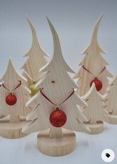 three wooden christmas trees with red ornaments on them and one has a gold ornament hanging from the top