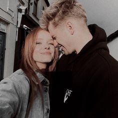 a man and woman standing next to each other with their faces close together in front of a building