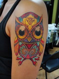 an owl tattoo on the upper arm and shoulder, with colorful flowers around its eyes