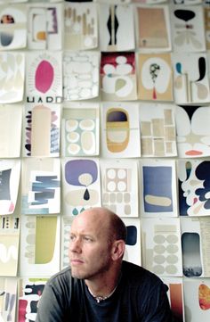 a man sitting in front of a wall covered with different types of paper cutouts