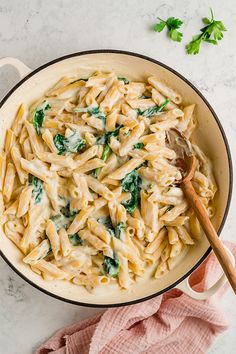 a skillet filled with pasta and spinach on top of a white marble counter