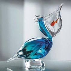 a glass bird figurine with a goldfish in it's beak sitting on a table