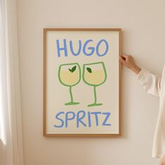 a woman standing next to a painting with two glasses on it that says hug spritz