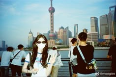 a group of people standing next to each other near the water with buildings in the background