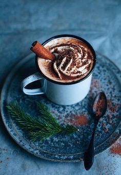 a cup of hot chocolate on a plate with cinnamon stick and sprig of rosemary