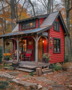 a small red cabin in the woods with lots of trees and leaves on the ground