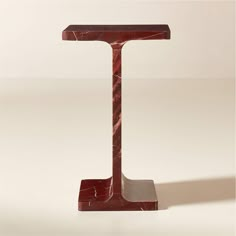 a red marble letter t stands on a white surface with a shadow from the floor