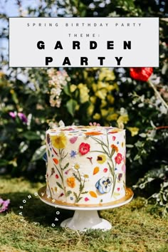 a birthday cake sitting on top of a lush green field with flowers in the background