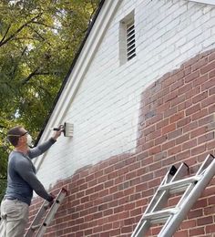 a man on a ladder painting the side of a brick building while another man stands next to him