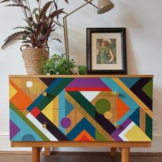 a colorful chest of drawers sitting on top of a wooden floor next to a potted plant