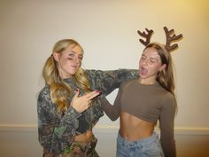 two young women standing next to each other in front of a white wall with deer antlers on it