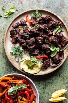 two plates filled with meat and vegetables on top of a green tablecloth next to a bowl of rice