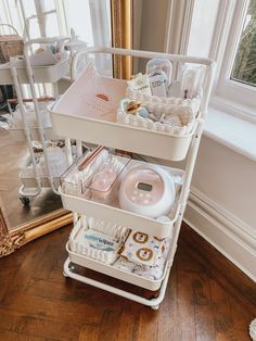 a three tiered cart filled with baby items in front of a large mirror on the floor