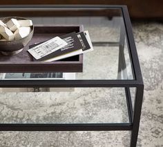 a glass and metal table with a bowl on it, some books and a remote control