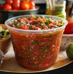 a plastic container filled with salsa sitting on top of a table next to other food