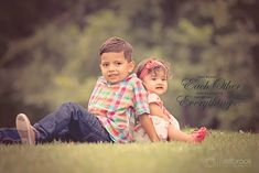 two young children sitting on the grass in front of trees