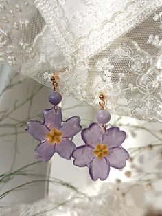 two purple flowers are hanging from the side of a white lace covered curtain with gold accents