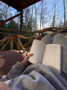 a person laying down reading a book in the hammock with trees in the background