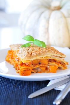 a white plate topped with lasagna covered in cheese and sauce next to silverware