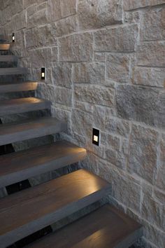 some stairs with lights on them next to a stone wall