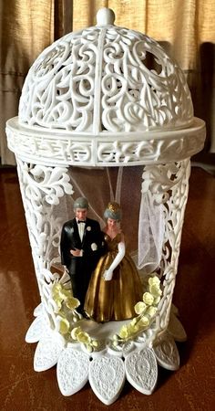 a wedding cake topper with a bride and groom in a white birdcage