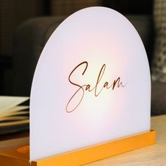 the name salam is written on a white light up sign that sits on top of a wooden table