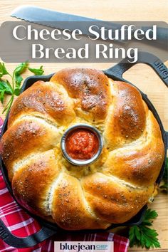 a loaf of bread in a cast iron skillet on a wooden table with a red and white checkered napkin