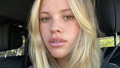 a blonde woman sitting in the back seat of a car looking at the camera with a serious look on her face