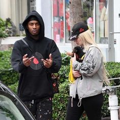 a man and woman standing next to each other in front of a car on the street