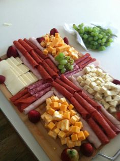 an assortment of cheeses and meats on a cutting board with grapes, celery